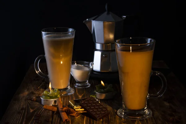 Dos vasos con latte, leche, chocolate y especias en una mesa de madera a la luz de las velas . — Foto de Stock