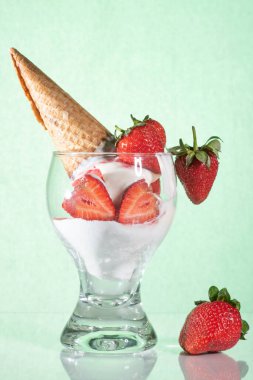Cam bir masanın üzerinde beyaz çilekli dondurma ve waffle külahı. Yeşil arkaplan