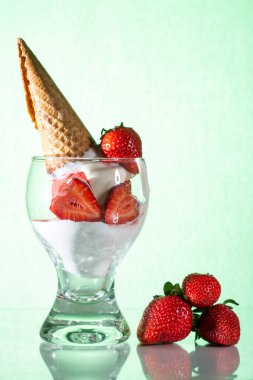 Cam bir masanın üzerinde beyaz çilekli dondurma ve waffle külahı. Yeşil arkaplan.