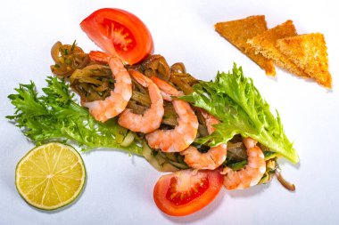Haşlanmış sebzeli karides ve beyaz bir yüzeye salatalık, domates ve limon dilimi ile marul. Üst görünüm.
