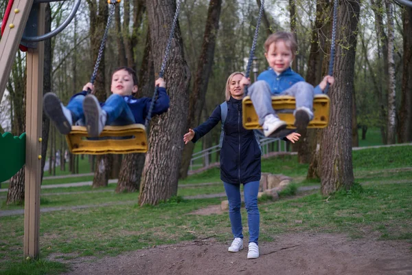 Mutter schwingt zwei Söhne im Herbst auf Schaukel im Park — Stockfoto