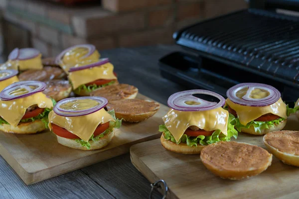 Velsmagende burgere med ost, salat, løg og tomater serveret udendørs på et træbord . - Stock-foto