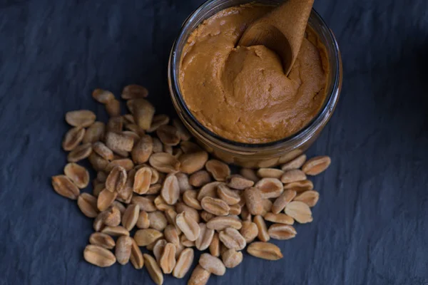 Bowl of peanut butter and peanuts on dark background — Stock Photo, Image