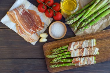 Parma jambonu bir kesme tahtası üzerinde sarılı taze organik kuşkonmaz