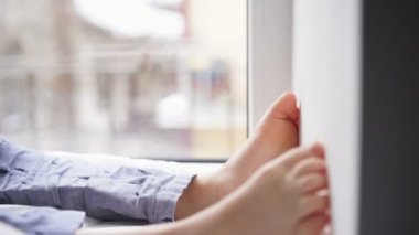 Pencere pervazına üzerinde oturan çocuk bir akıllı telefon kullanır