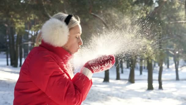 Дівчина в червоних ударах в долонях снігу в теплому заході сонця — стокове відео