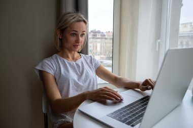 Büyük pencere kahve ile oturma ve dizüstü bilgisayarda çalışan genç çekici kız.