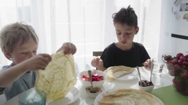De jongens pannenkoeken met aardbeien in buis oprollen. Jongens pannenkoeken eten. — Stockvideo