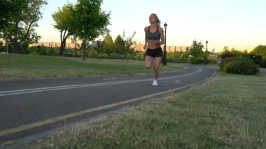 Genç çekici atletik kadın ağır çekimde gün batımında Park'ta jogging
