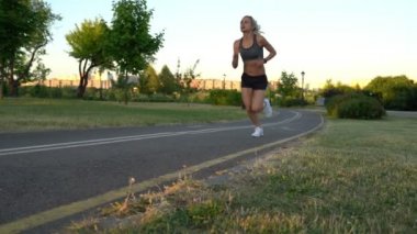 Genç çekici atletik kadın ağır çekimde gün batımında Park'ta jogging