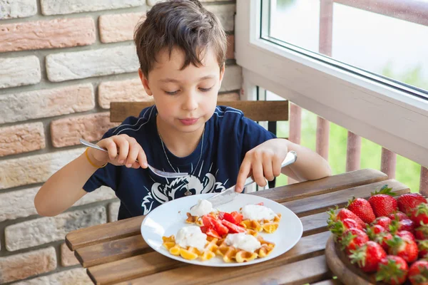 Dos chicos están comiendo gofres con fresas y helado sobre una mesa de madera en el balcón — Foto de Stock