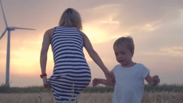 Madre e hijo caminando en campo de trigo con turbinas eólicas — Vídeo de stock