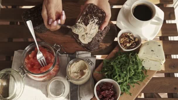 Kvinnlig hand att göra smörgås med hummus och lax för frukost. Ovanifrån. Solig dag — Stockvideo