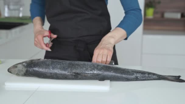 Женщина режет рыбу ножом на кухне — стоковое видео