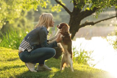 Güzel genç bir kadın sonbaharda parkta köpeğiyle oynuyor.