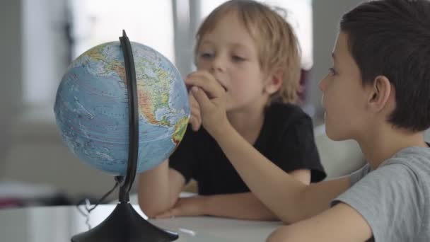 Two caucasian boys spin a globe and dream about travel. — Stock Video