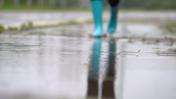 Close-up van vrouw in blauw rubber laarzen springen op de plas — Stockvideo