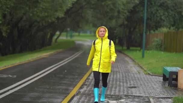 Mutlu bir güzel genç kadın yağmur zevk sarı yağmurluk içinde. — Stok video