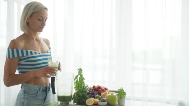 Mujer bebiendo batido de verduras verdes en la cocina. Estilo de vida saludable — Vídeos de Stock