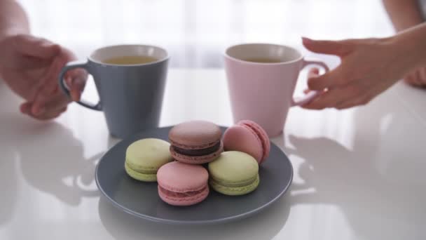 Close up of male and female hands holding cups of coffee with macaroons are on table — Stock Video