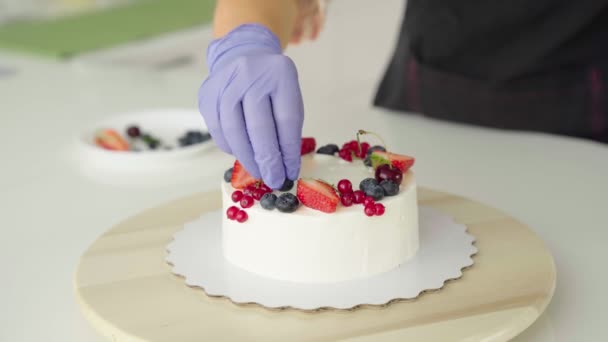 La chica, la principal pastelera, decora bayas del bosque, fresas, un pastel casero — Vídeo de stock