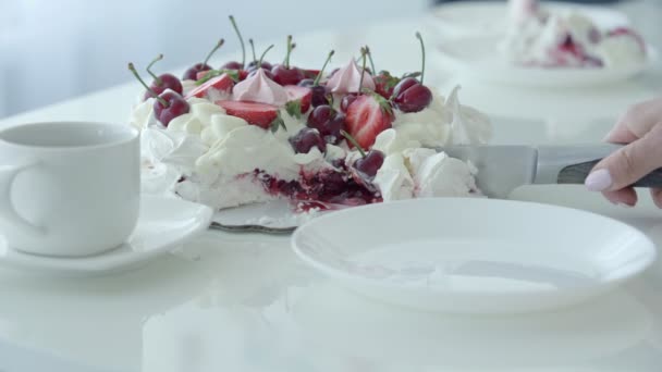 Самка вручную режет десерт и кладет его на белую тарелку. Белый торт с ягодами. Павловский десерт — стоковое видео