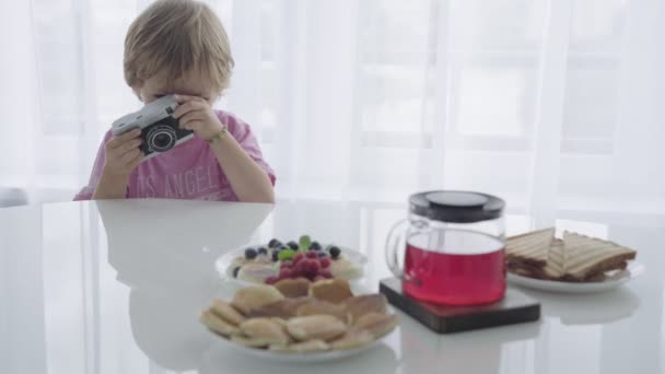 Mãe está preparando café da manhã e neste momento o menino interpreta o fotógrafo — Vídeo de Stock