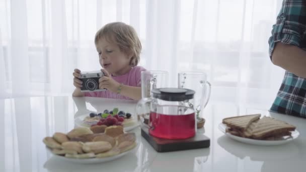 Maminka se připravuje snídani a v současné době chlapec hraje fotograf — Stock video