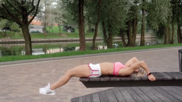 Young woman doing abs crunches in park on a bench — Stock Video