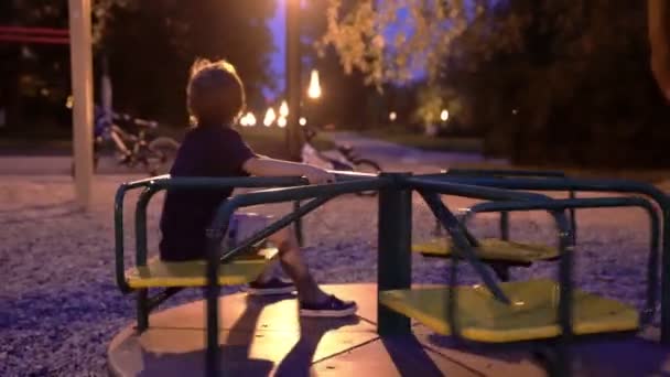 オープンエアの夜を楽しむ遊び場で二人の少年。男の子は、夜 otdoors を遊んでいます。 — ストック動画