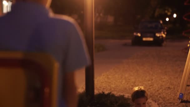 Két fiú élvezi a szabadban éjjel játszótéren. Fiúk játszanak otdoors éjszaka — Stock videók