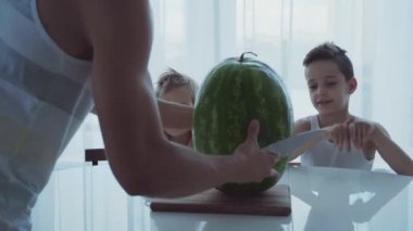 Bir akşam yemeği masada oturan iki küçük komik çocuklu aile. Babam büyük bir karpuz keser.