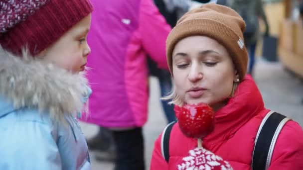 Jonge vrouw bijt een karamel appel op de kerstmarkt — Stockvideo