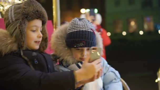 Два мальчика делают селфи на площади возле рождественской елки — стоковое видео