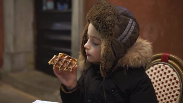 Niño comiendo gofres belgas con chocolate en la calle — Vídeo de stock