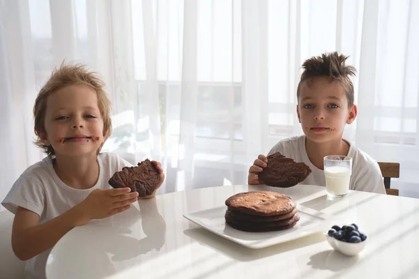 Two cute boys sitting on kitchen eating cookies and talking — Stock Photo, Image