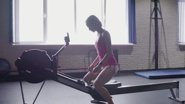 Jeune femme athlétique faisant de l'entraînement à la machine à ramer au gymnase — Video