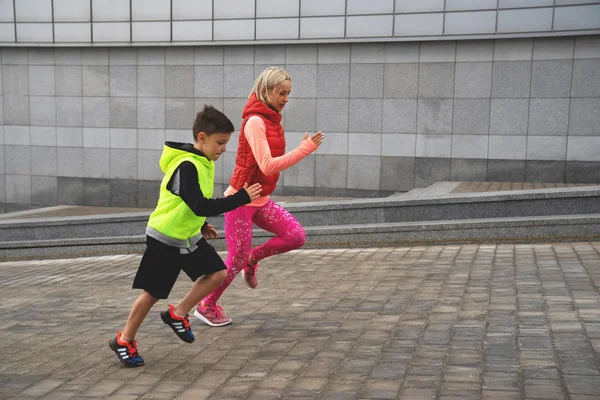 Спортсменка та хлопчик бігають на тлі міського ландшафту. Сімейний спорт . — стокове фото