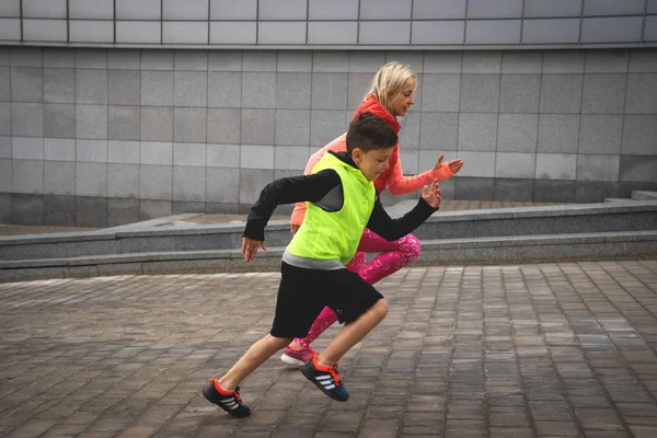 Athletic young woman and boy are running on background of urban landscape. Family sport. — Stock Photo, Image