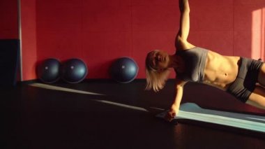 Kadının bir tarafı tahta mavi mat karın egzersiz yapması. Fitness hakkında bu Video. Günbatımı ışık