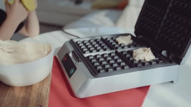 Jovem mulher cozinhar waffles na cozinha e bonito menino ajuda-a — Vídeo de Stock