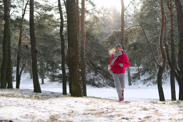 Vrouwelijke atleet joggen in koude winter forest het dragen van warme sportief uitgevoerd kleding en handschoenen. — Stockfoto