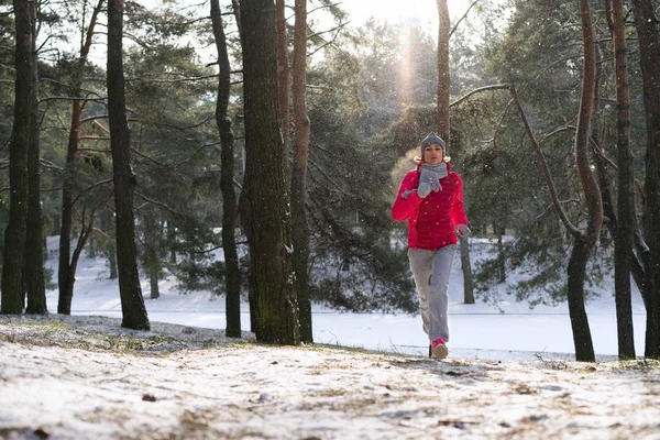 Vrouwelijke atleet joggen in koude winter forest het dragen van warme sportief uitgevoerd kleding en handschoenen. — Stockfoto