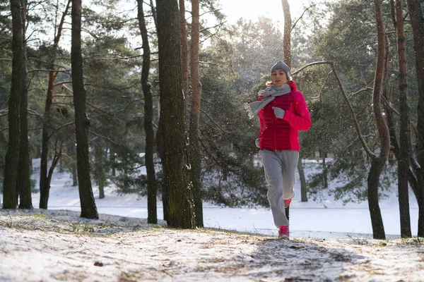 Female runner jogging in cold winter forest wearing warm sporty running clothing and gloves. — Stock Photo, Image