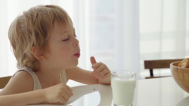 Мальчик ест домашнее печенье с молоком на домашней кухне — стоковое видео