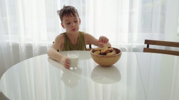 Niño comiendo galletas caseras con leche en casa cocina — Vídeos de Stock