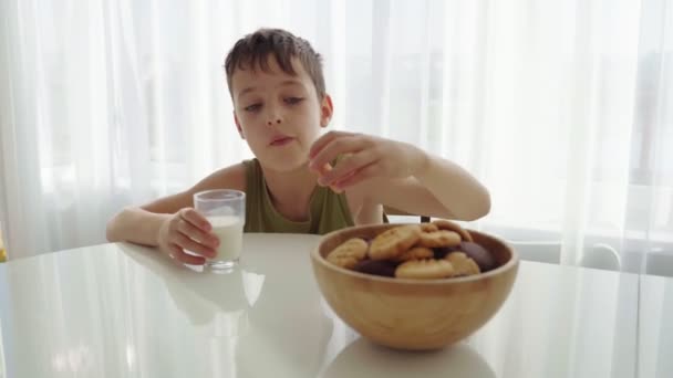 Niño comiendo galletas caseras con leche en casa cocina — Vídeo de stock