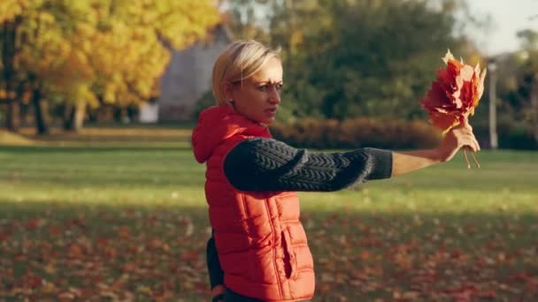 Mujer joven sosteniendo hoja de arce amarillo en otoño amarillo fondo soleado en el parque de otoño — Vídeos de Stock