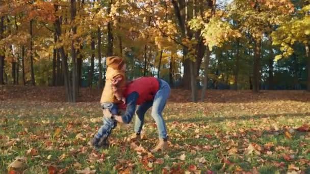 Moeder en peuter zoon spelen samen met de gevallen bladeren in de herfst park of bos. Moeder is het gooien van bladeren in de lucht. — Stockvideo