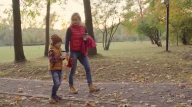 Anne ve bebek son sonbahar park veya ormanında düşen yapraklar birlikte çalacak. Anne yaprakları havada atıyor